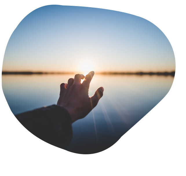 Hand reach towards a sunrise. The sun is reflecting off a lake.