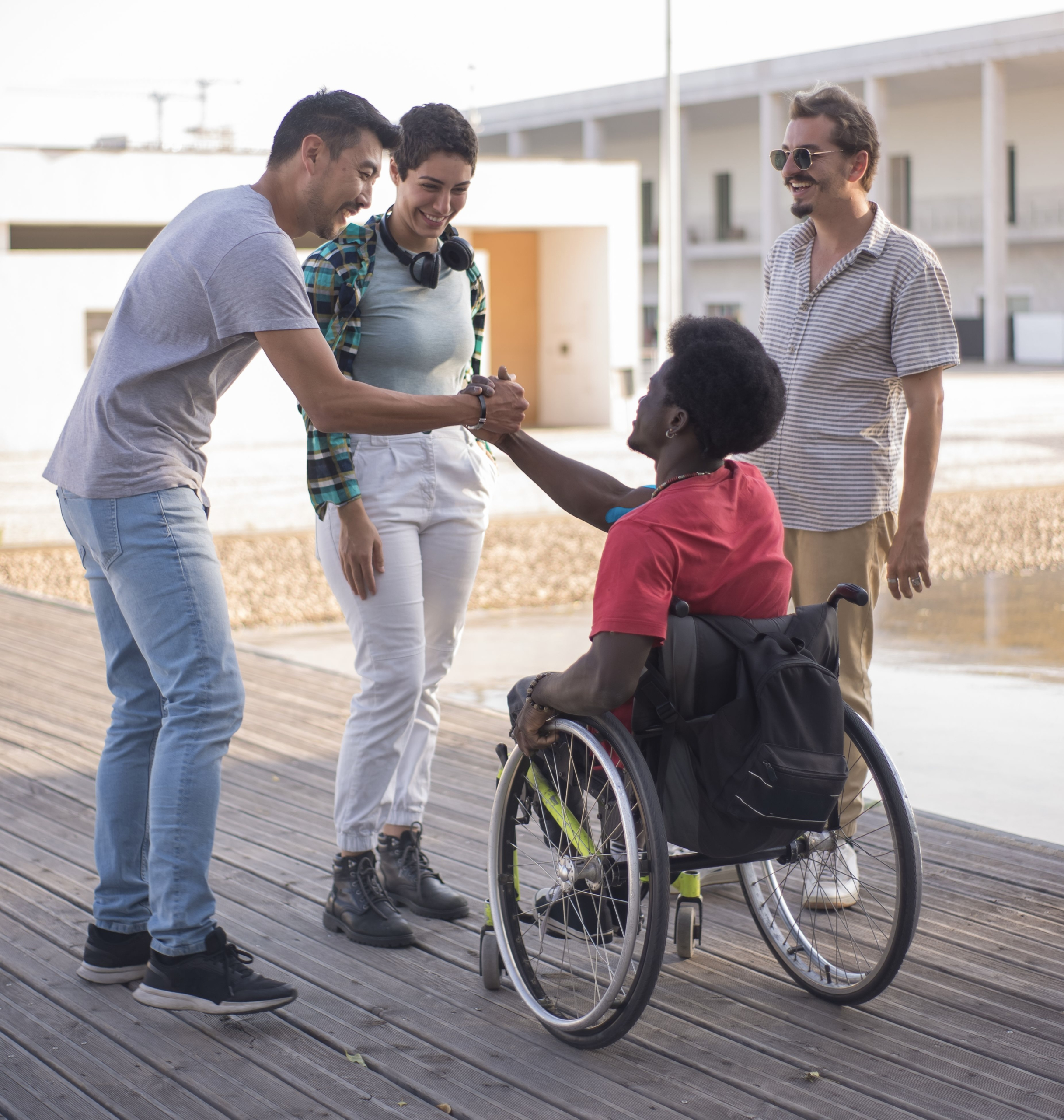 A wheelchair user greeting another person outdoors while two others stand nearby.