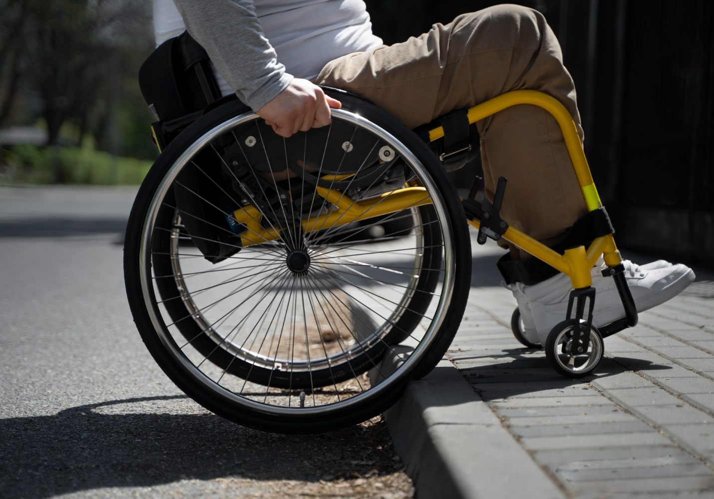 A person in a wheelchair attempting to push themselves up to a sidewalk from the street. Their front two wheels are on the sidewalk.